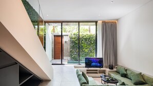 A modern living room with a green sofa, a flat-screen TV, and a staircase leading to an outdoor area. - Coco Jungle Canggu Villas by Nagisa Bali (Canggu)