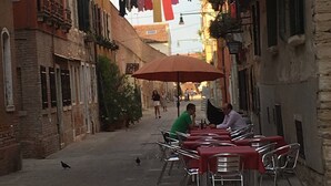 A narrow street with outdoor seating, a red umbrella, and hanging laundry. - Painters House Biennale Arsenale (Venice)