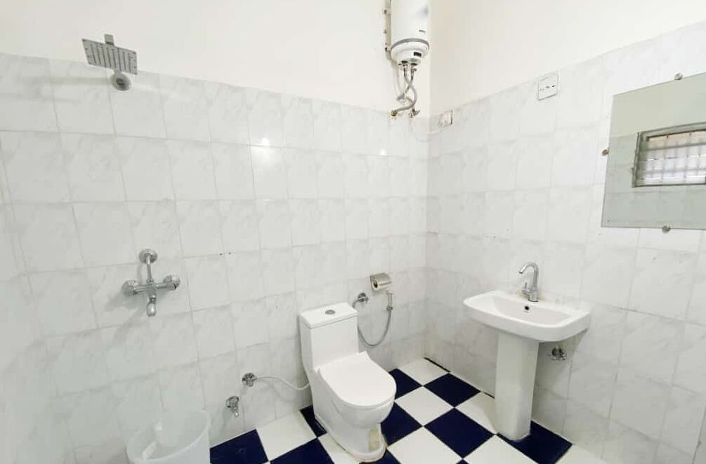 A bathroom with white tiles, a toilet, a sink, and a shower.