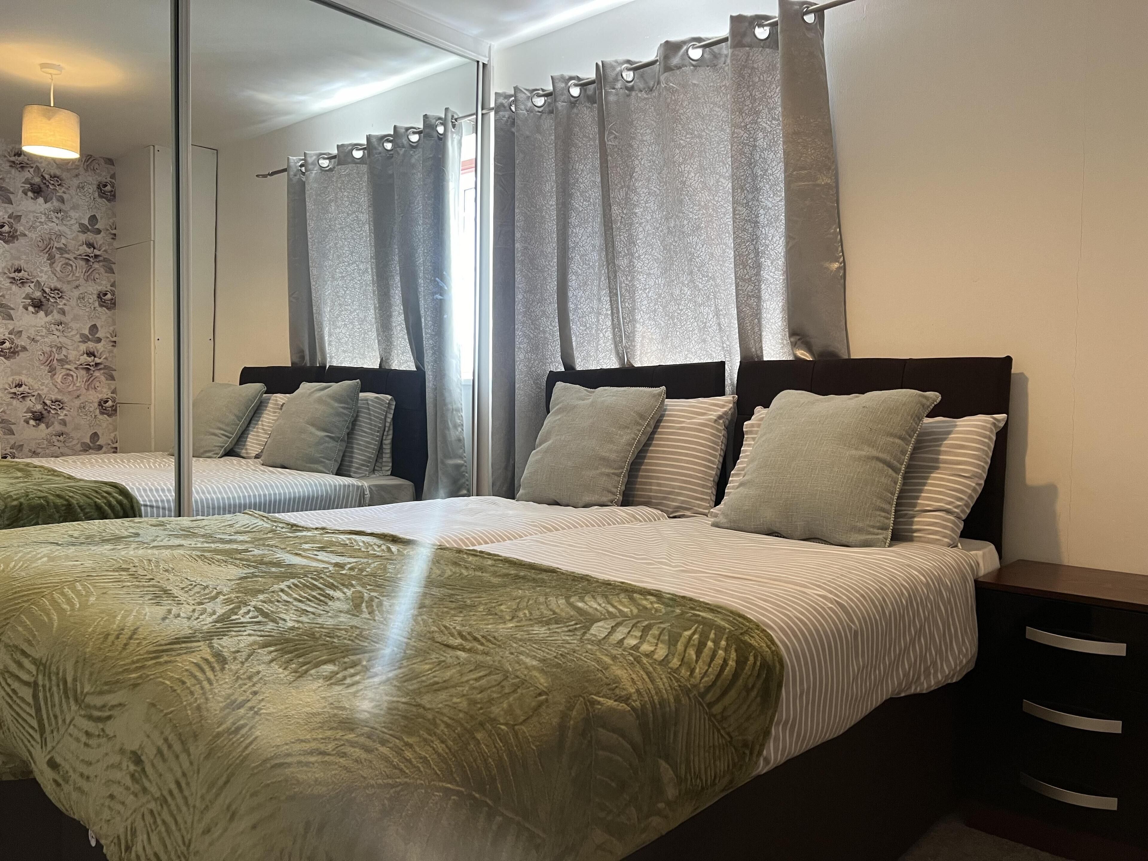 A bedroom with a mirrored wall, two beds with striped bedding, and a green patterned bedspread.