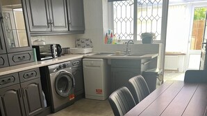 Una cocina con armarios grises, lavadora, lavavajillas y una mesa de comedor con sillas.