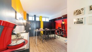 A modern kitchen with a red coffee machine, a dining area with a black table and chairs, and a yellow accent wall. - Chambre privative rouge (Mulhouse)