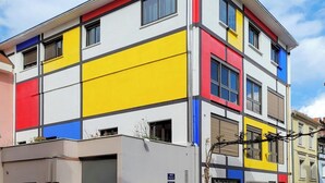 A multi-story building with a modern design, featuring a mix of white, yellow, red, and blue panels. - Chambre privative rouge (Mulhouse)