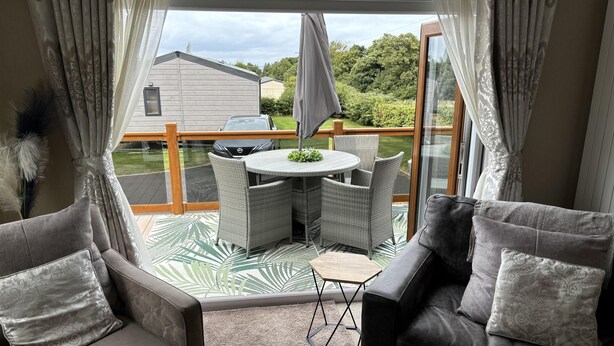 Un espace patio moderne avec des meubles en osier, une table ronde et une vue sur une maison et la verdure.