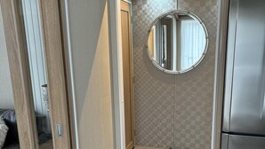Une salle de bain moderne et compacte, dotée d’un meuble-lavabo en bois, d’un miroir rond et d’un réfrigérateur encastré en acier inoxydable.