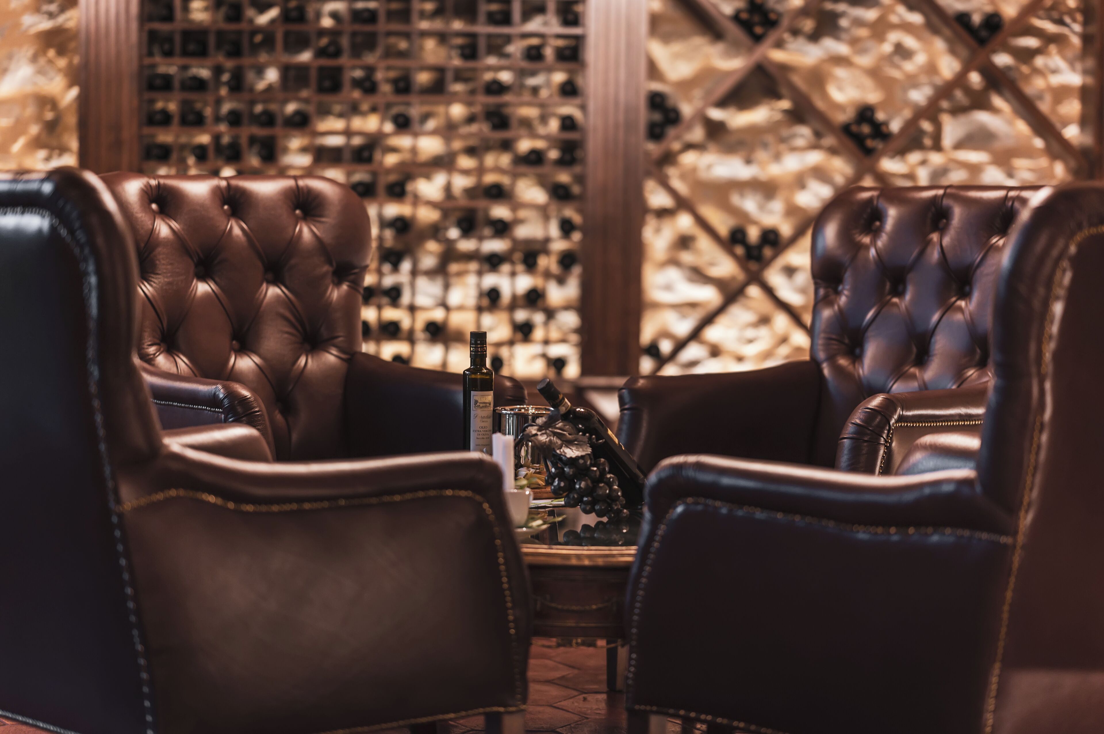 A luxurious seating area with leather chairs and a wine rack in the background.
