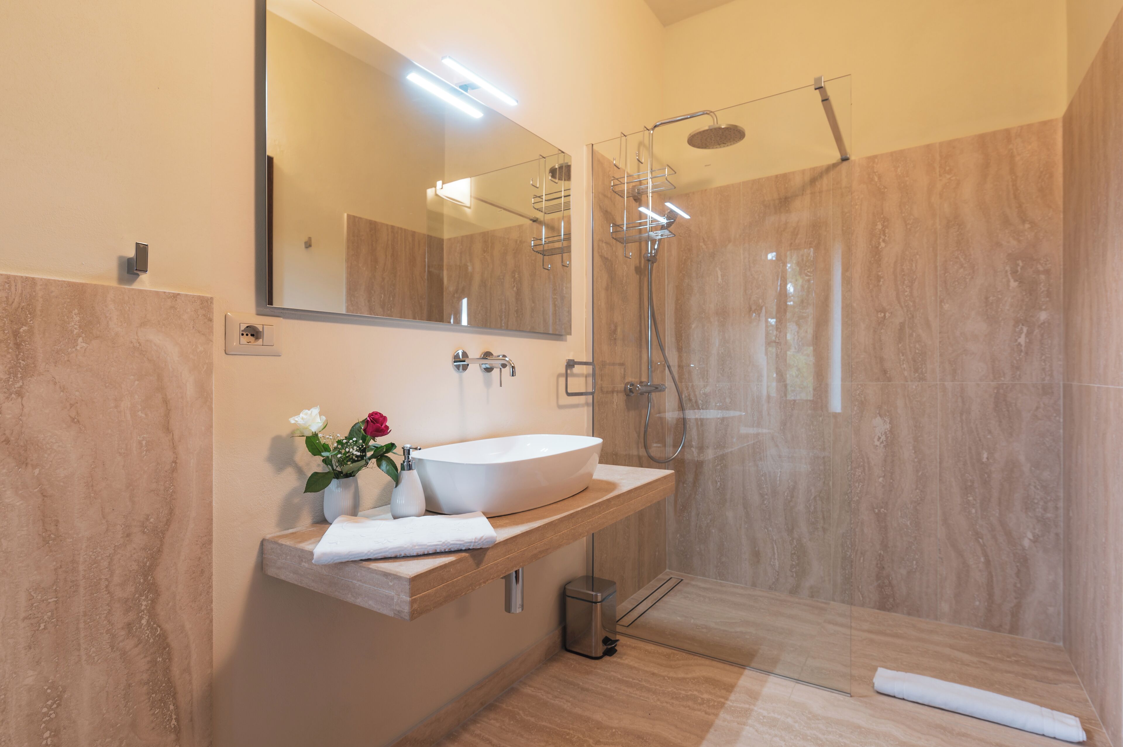 Ein modernes Badezimmer mit großem Spiegel, einem Händewaschbecken, einer Duschkabine und einer Wand mit Marmorplatten.
