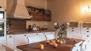 Een moderne keuken met witte kasten, een houten eettafel en een vaas met bloemen.