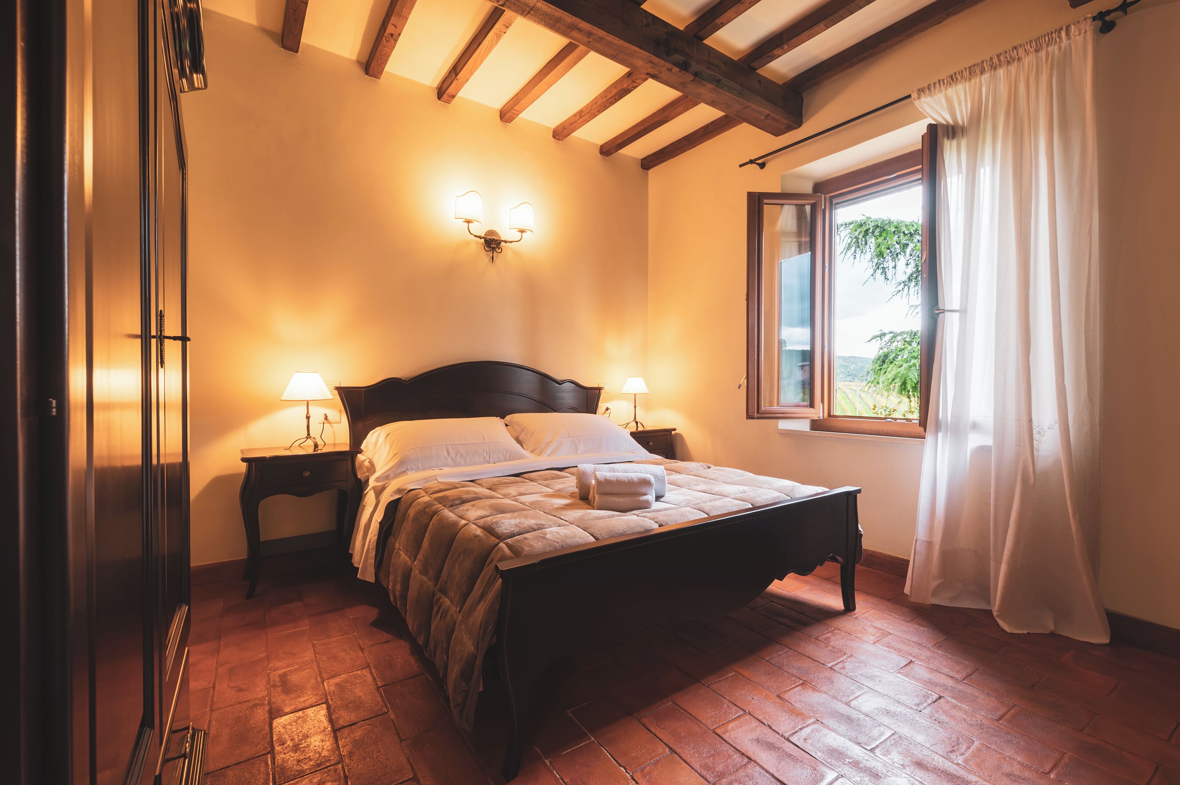Une chambre à coucher avec un lit en bois, deux tables de chevet, une fenêtre avec des rideaux et un luminaire fixé au mur.