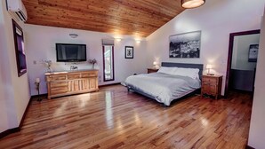 Una camera da letto con soffitto in legno, un letto, una cassettiera, una televisione e una finestra.