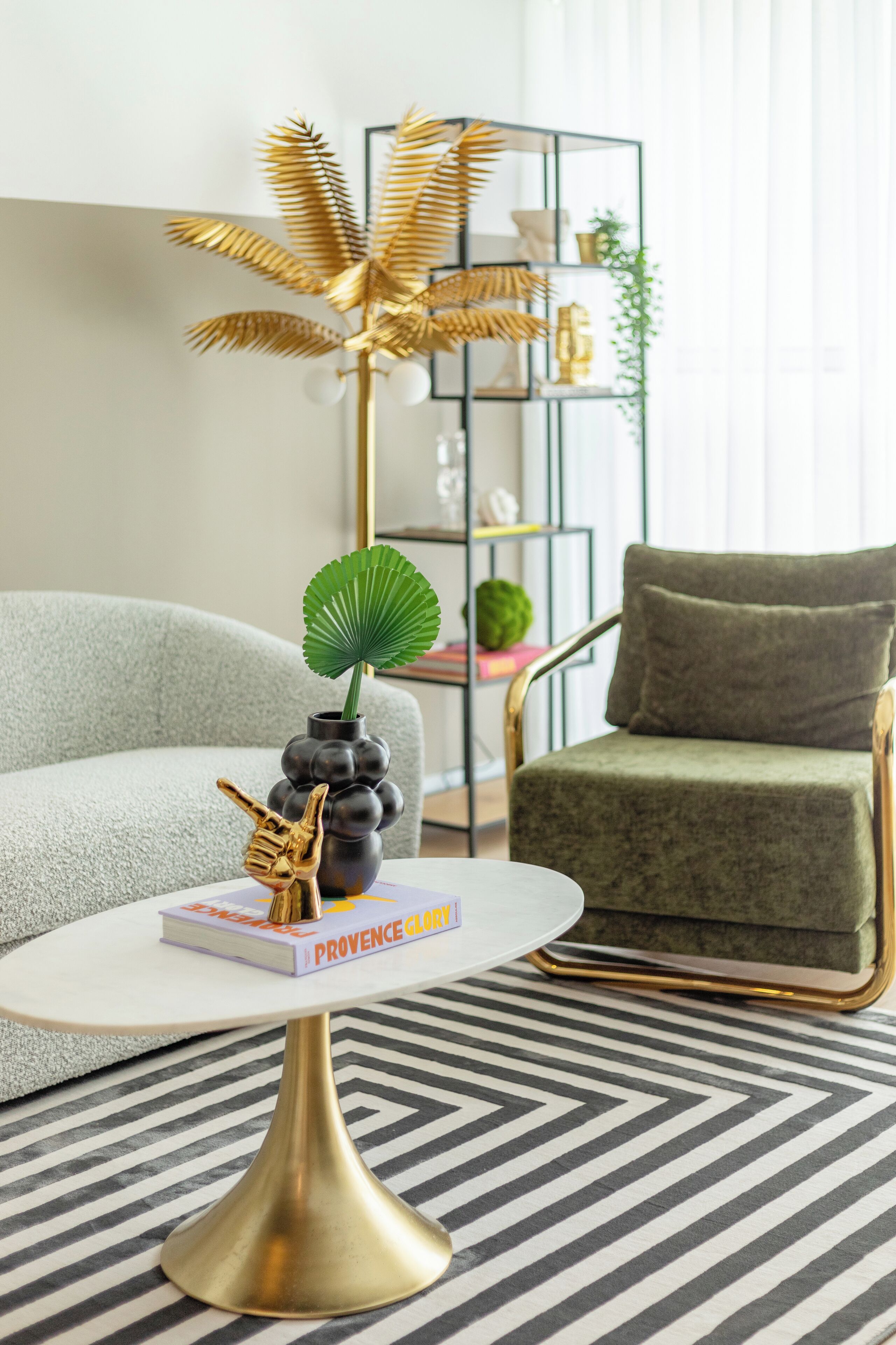 A modern living room with a white round table, a green armchair, and a gold floor lamp.