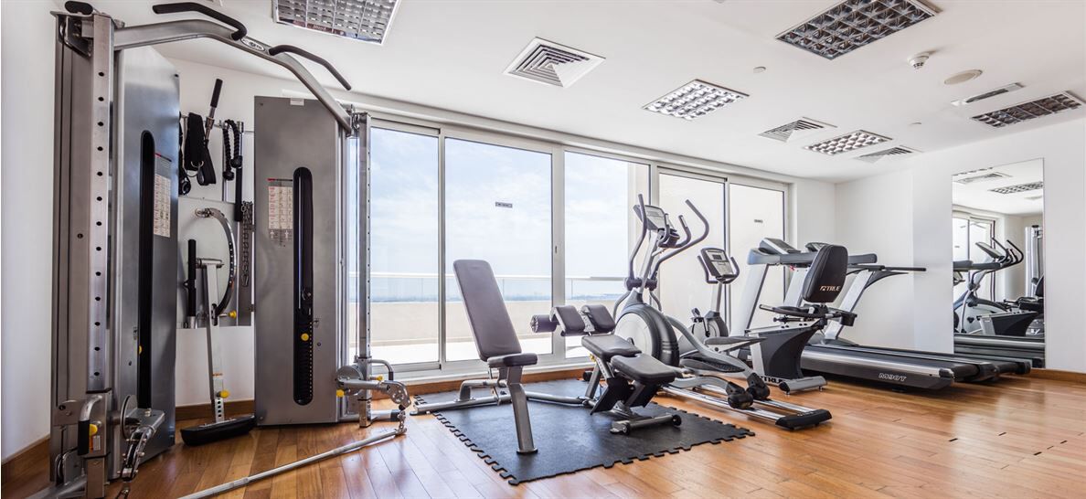 A gym with cardio machines, weightlifting equipment, and a large window offering a view.