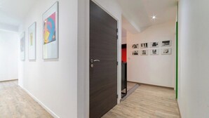 Ein Flur mit einer dunklen Holztür, gerahmten Kunstwerken an den Wänden und einem Holzboden.
