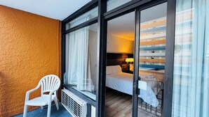 Une chambre d’hôtel avec un lit, une table de chevet, une lampe et une vue sur un immeuble par la fenêtre.
