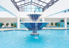 Un'ampia piscina interna con una fontana al centro, circondata da sedie bianche e piante in vaso.