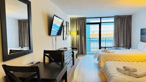 Une chambre d’hôtel avec un lit, un bureau, une chaise, une télévision et une fenêtre avec des rideaux.