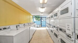 A laundry facility with rows of washing machines and dryers, a yellow wall, and a door leading outside. - LA82 Beautiful Studio on the beach + pool+ hot tub (Myrtle Beach)