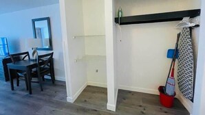 A room with a dining table and chairs, a small kitchen area, a built-in shelf with a towel, and a mop leaning against the wall. - LA82 Beautiful Studio on the beach + pool+ hot tub (Myrtle Beach)
