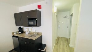 Cocina compacta con armarios oscuros, microondas, cafetera y fregadero.