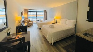Una habitación de hotel con dos camas, un escritorio, una silla y un amplio ventanal con vistas.
