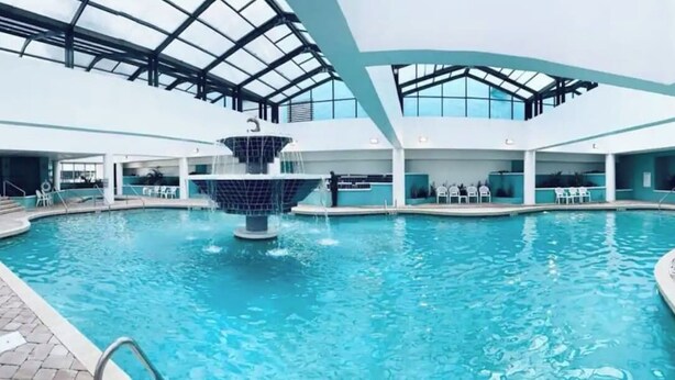 An indoor swimming pool with a central fountain, surrounded by lounge chairs and a covered seating area. - LA105 Amazing Ocean View studio on the beach+ pool (Myrtle Beach)