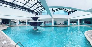 An indoor swimming pool with a central fountain, surrounded by lounge chairs and a covered seating area. - LA105 Amazing Ocean View studio on the beach+ pool (Myrtle Beach)
