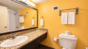 A bathroom with a granite countertop sink, a mirror, a toilet, and two towel racks.