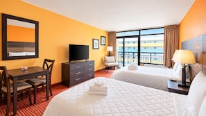 A hotel room with two beds, a desk, a TV, and a view of a building.