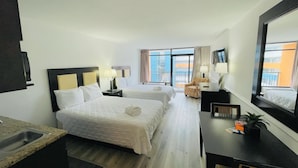 Ein Hotelzimmer mit zwei Betten, einem Schreibtisch, einem Stuhl, einem Spiegel und Blick auf die Stadt.