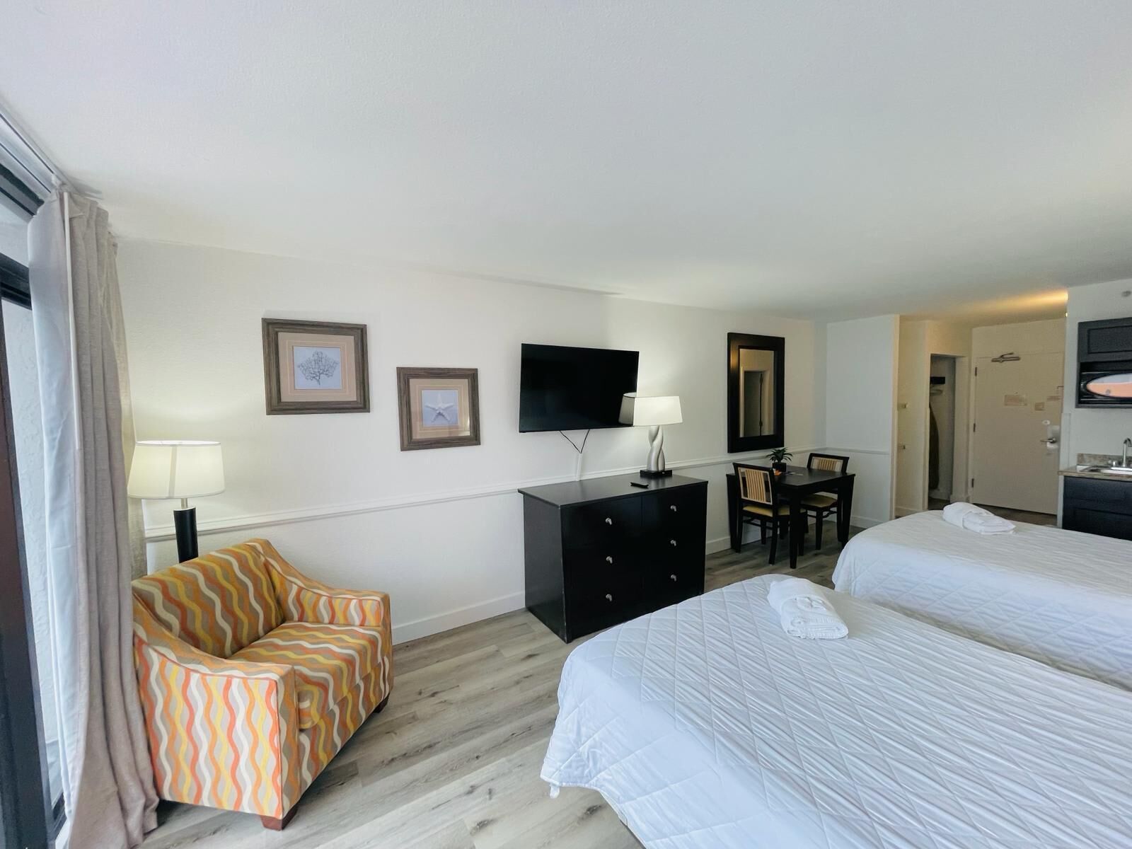 A hotel room with two beds, a desk, a chair, a TV, and a dresser.