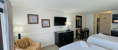 A hotel room with two beds, a desk, a chair, a TV, and a dresser.