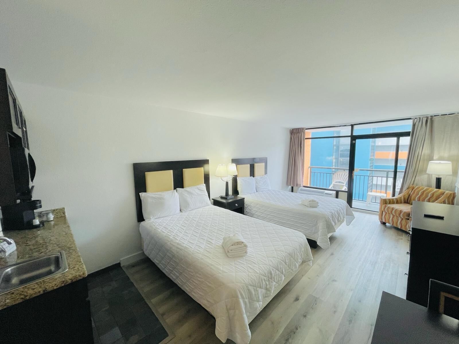 A hotel room with two beds, a desk, a chair, a balcony with a view, and a large window.