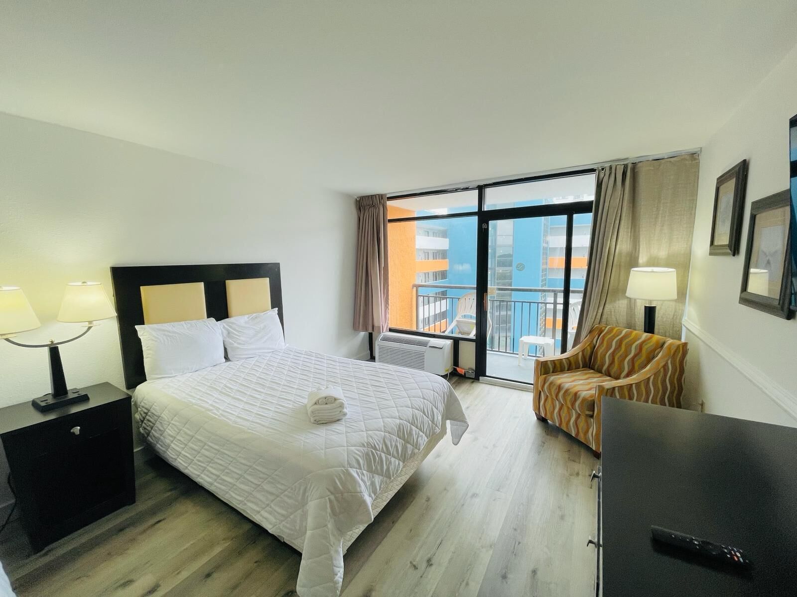 Ein Hotelzimmer mit Bett, Stuhl, Schreibtisch und Blick auf die Stadt durch große Fenster.