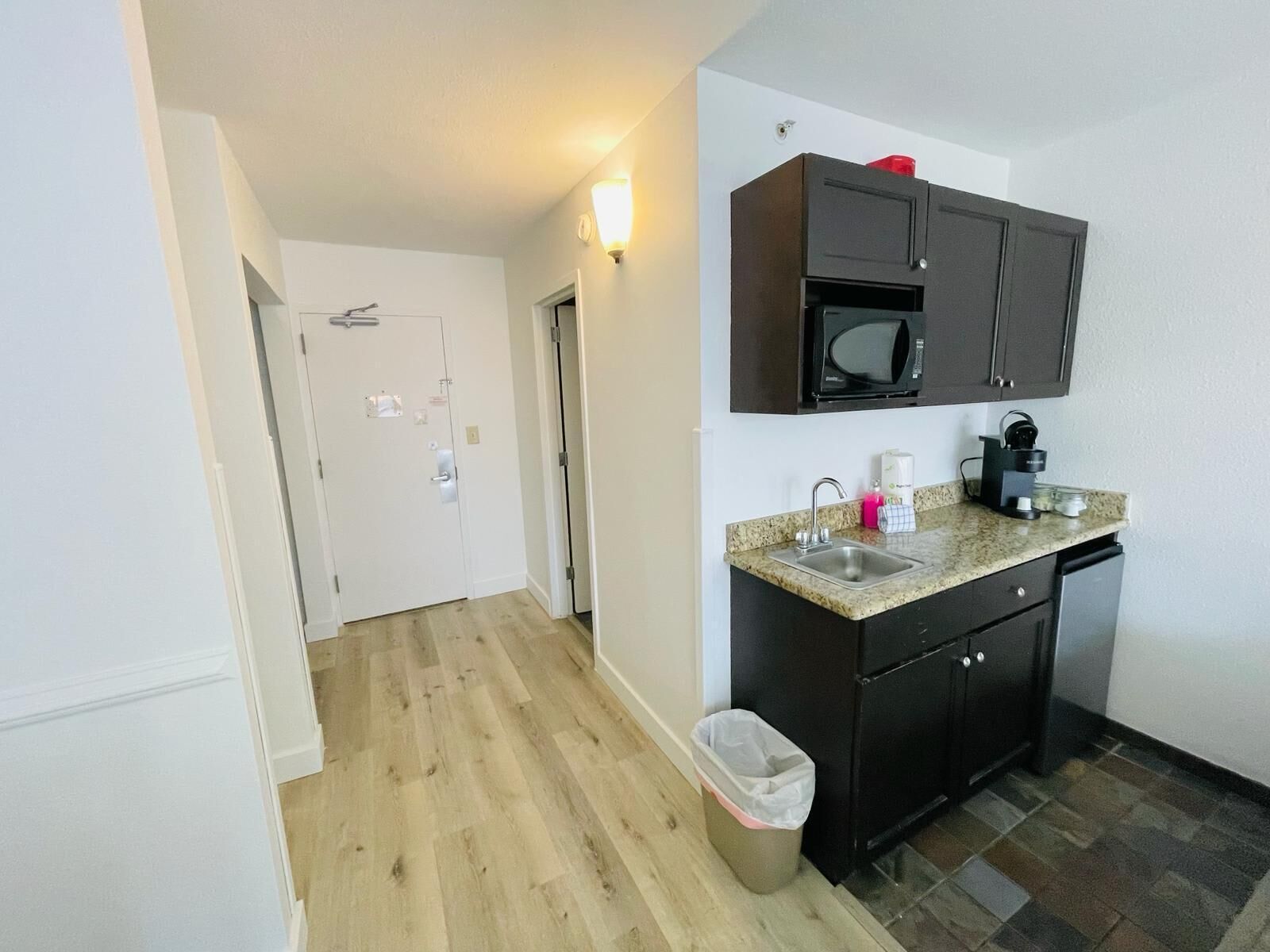 A compact kitchen with dark cabinets, a microwave, a coffee maker, and a granite countertop.