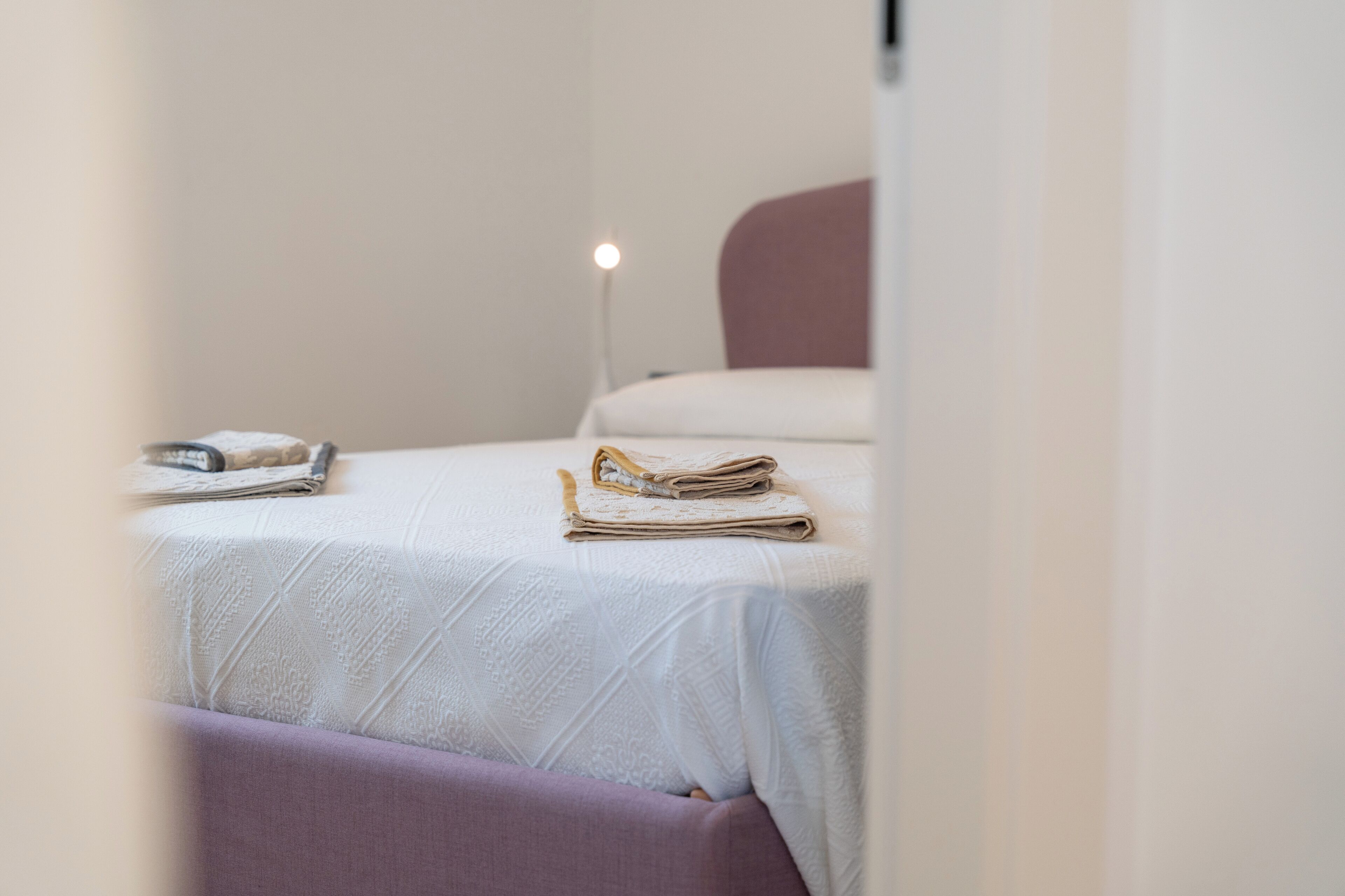 A neatly made bed with a folded towel and a book on the nightstand.