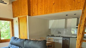A modern living room with a grey sofa, wooden ceiling, and a kitchen area with white cabinets and a dishwasher. - Racons del Pedraforca (Saldes)
