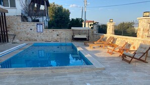 A swimming pool with lounge chairs and a stone wall. - Atlas homes (Demre)