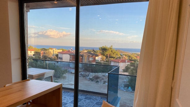 A balcony with a view of a residential area, a wooden table, and a beige sofa. - Atlas homes (Demre)