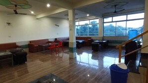 Um espaço amplo e arejado, com pé direito alto, diversos assentos, incluindo sofás e mesas, e grandes janelas que proporcionam iluminação natural.