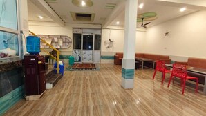 Um hall de hotel com piso de mármore, balcão de recepção, escada e cadeiras vermelhas.