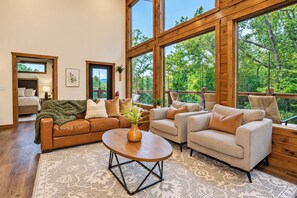 A spacious living room with a large window, a wooden floor, and a cozy seating area.