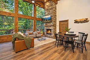 A spacious living area with a stone fireplace, large windows, and a dining set.