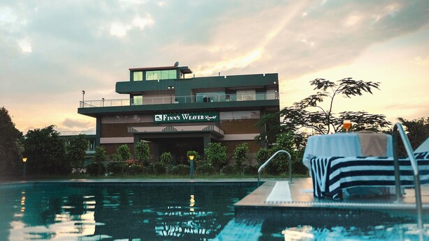 A modern hotel with a pool, a sign reading "Finn's Weaver Resort," and a sunset in the background.
