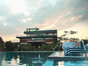 A modern hotel with a pool, a sign reading 'Finn's Weaver Resort,' and a reflection of the sky in the water. - Finns Weaver Resort Kaziranga (Bokakhat)