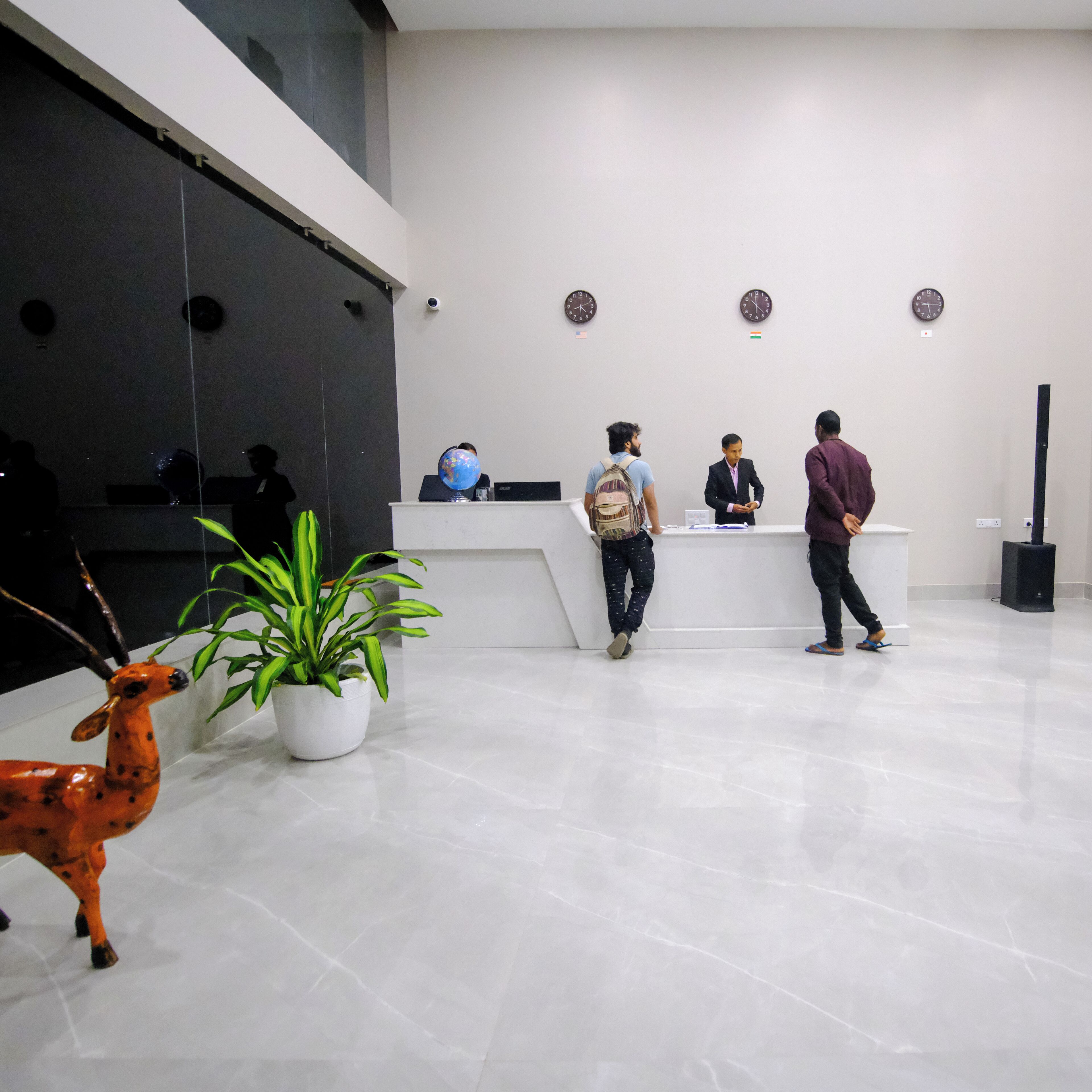 Un espace d’accueil avec un comptoir de réception blanc, une plante en pot et une statue d’antilope décorative.