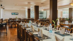 A spacious dining area with multiple tables and chairs, large wooden columns, and a modern chandelier.