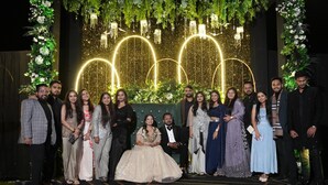 A group of people posing in front of a decorated backdrop with floral arrangements and illuminated arches.