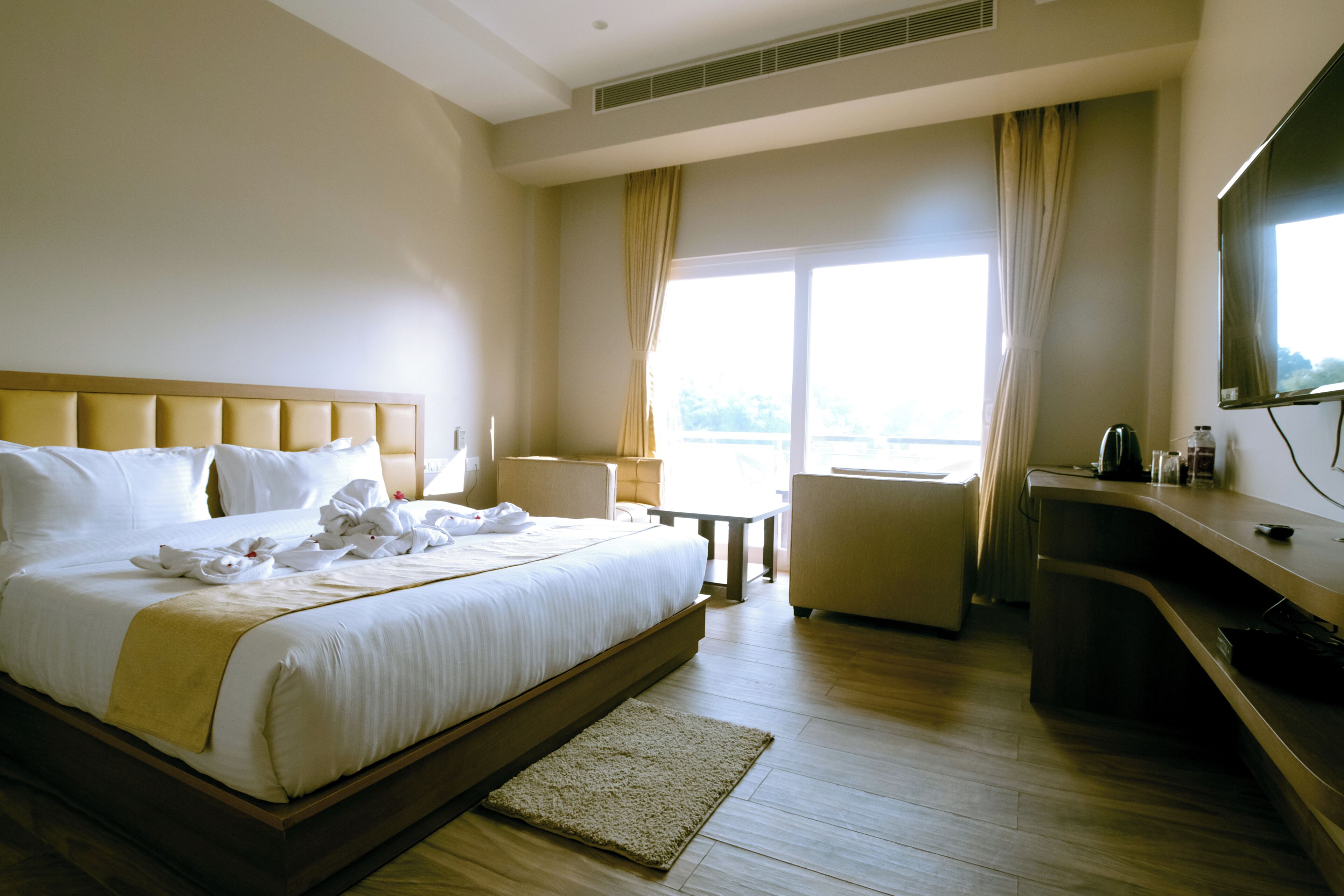 Quarto de hotel com uma cama grande, uma escrivaninha, uma cadeira e uma televisão.