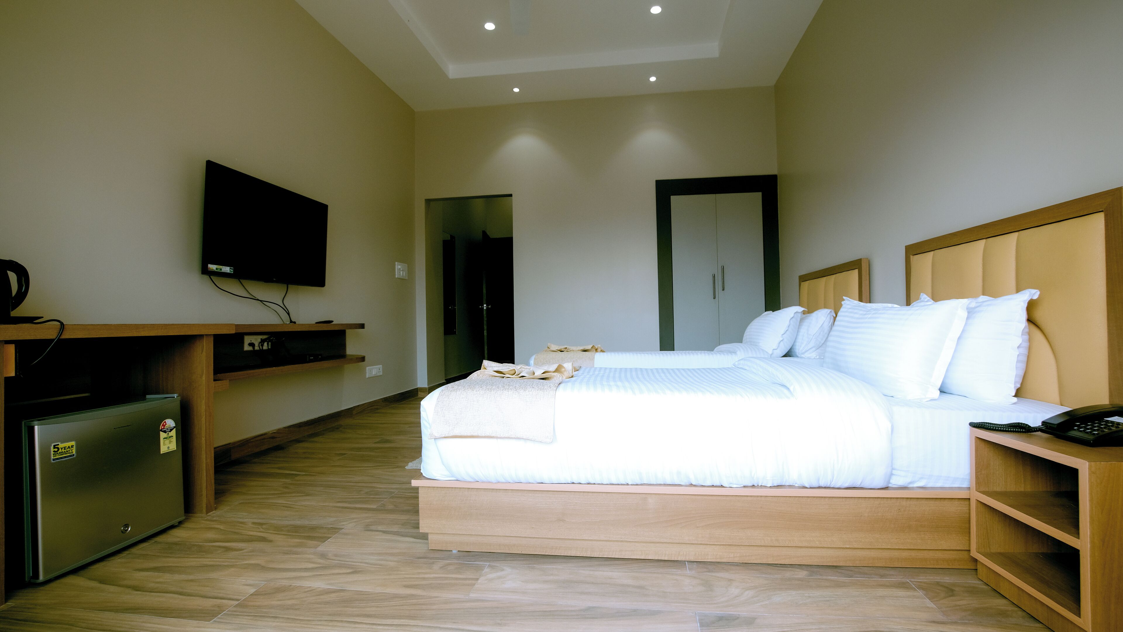 A hotel room with a bed, bedside table, TV, and a refrigerator.