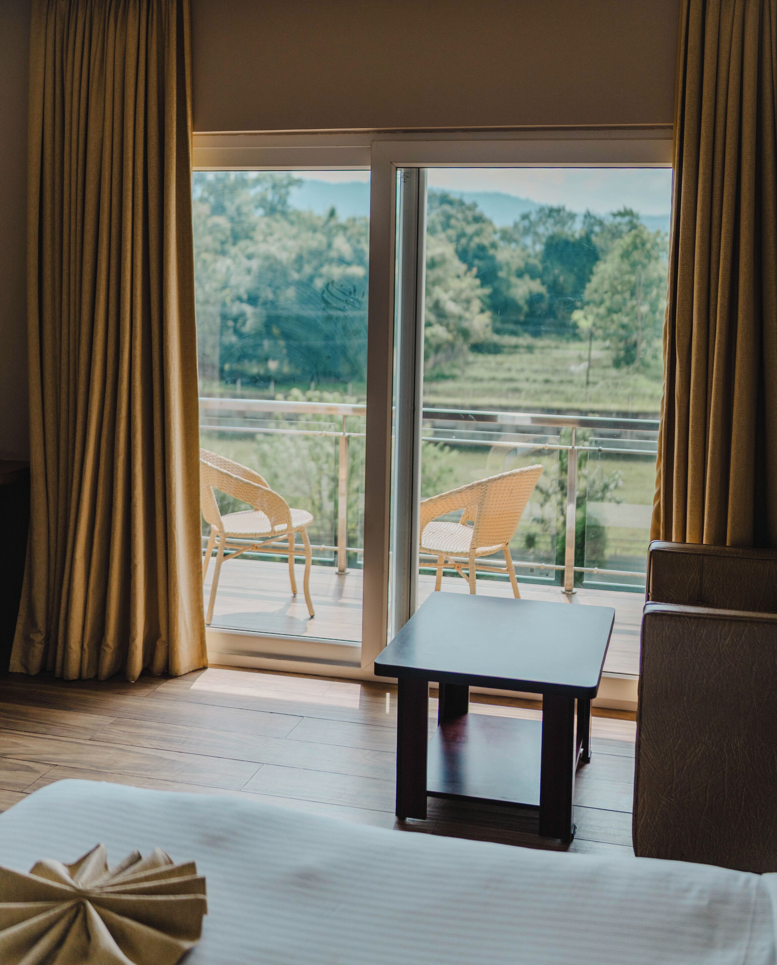 A hotel room with a large window, a bed, a table, and two wicker chairs.
